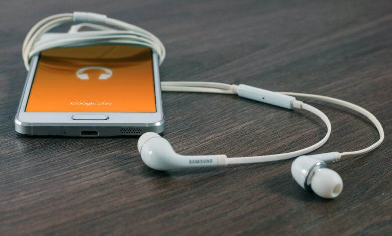 white Samsung Android smartphone turned beside white earbuds on brown board
