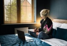 woman in purple and white floral long sleeve shirt and gray pants sitting on bed