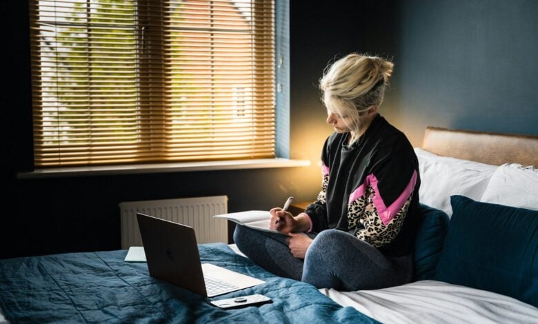 woman in purple and white floral long sleeve shirt and gray pants sitting on bed